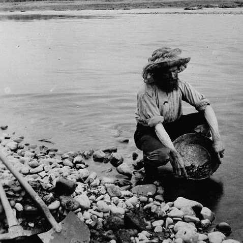 A black-and-white photo of a man panning for gold.