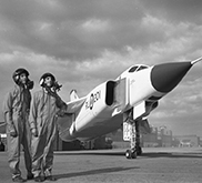 Black and white photograph of two men standing next to an airplane looking towards the horizon