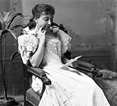 Black and white photograph of Émilie Lavergne wearing a pale dress, sitting in a chair and reading a letter.