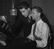 Black-and-white photograph of two men in front of a microphone.