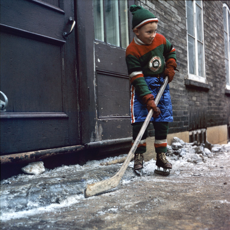 Boy with a hockey stick and skates, in front of a house, Quebec City