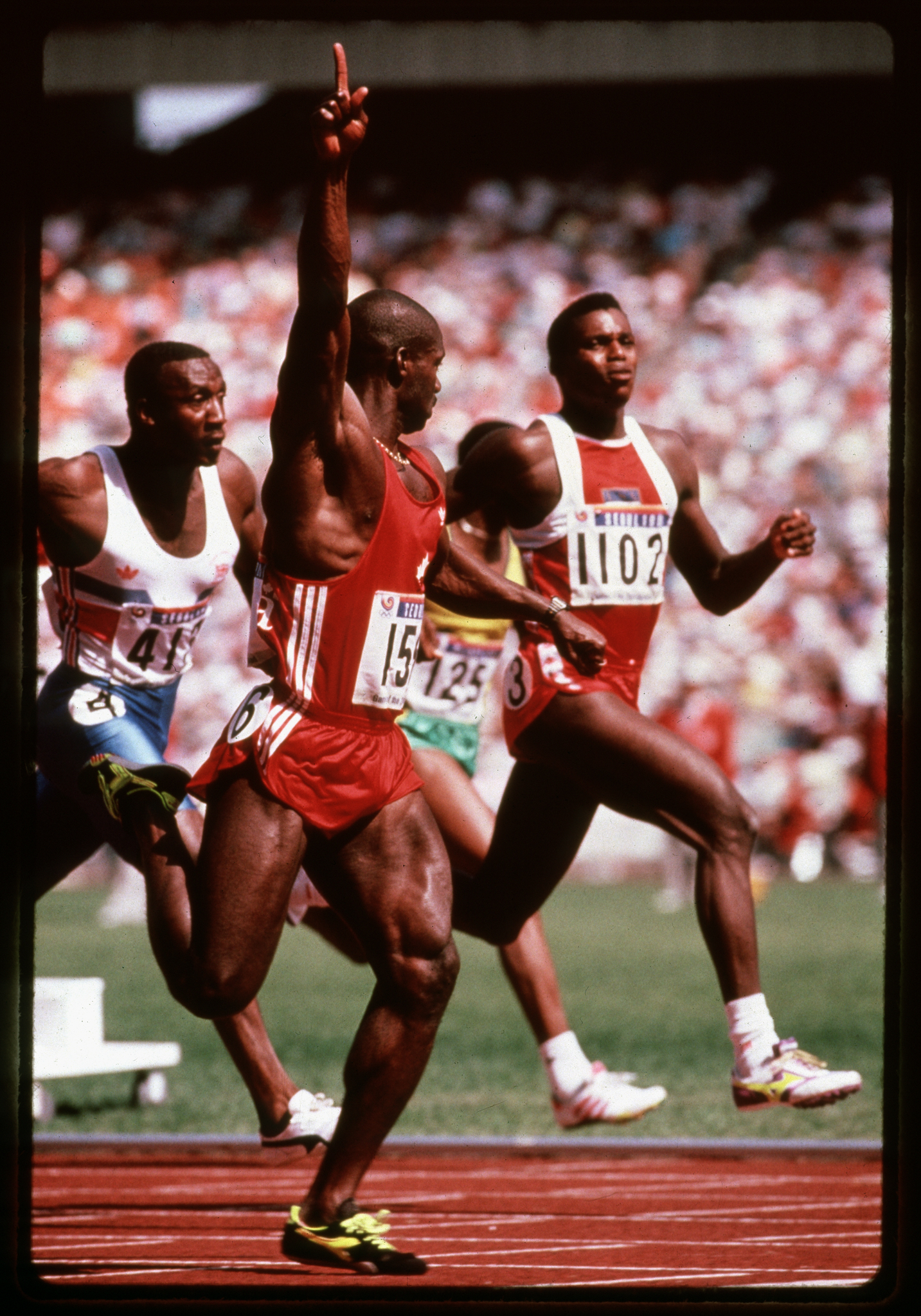 Runners in a race. Foreground runner looking back with arm pointed in the air.