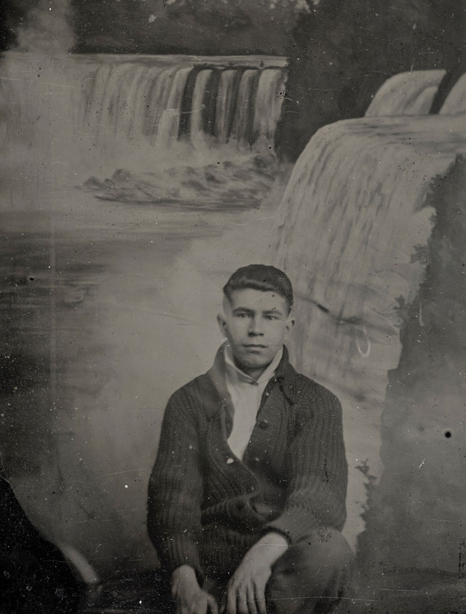 A young man seated with waterfalls in the background. Image is horizontally bent along centre.