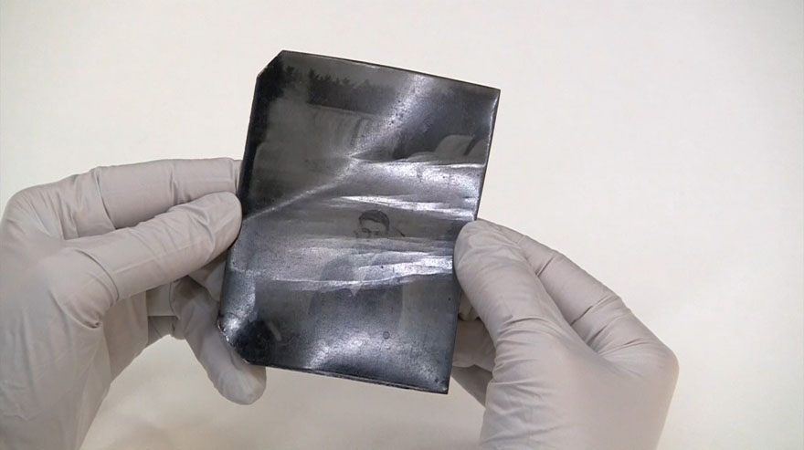 A close-up of hands rotating a tintype. Horizontal bends can be seen