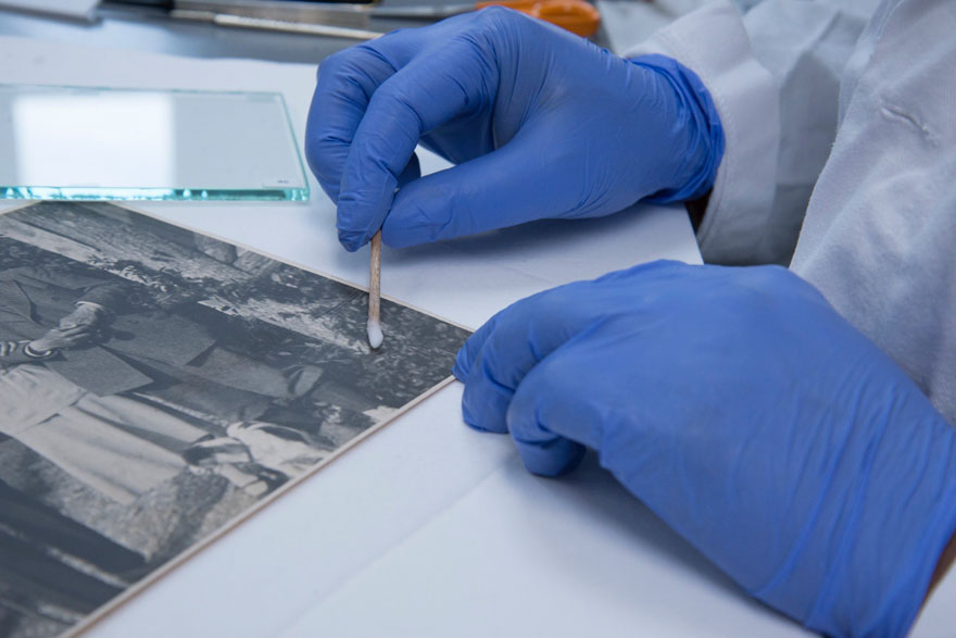 Two hands wearing blue gloves, rolling a cotton swab onto a photograph