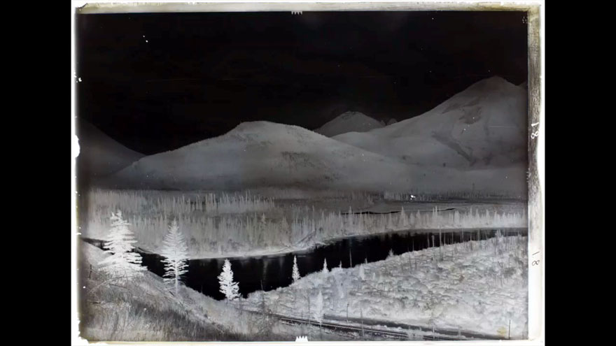 A negative of a landscape with mountains in the background and a river in the foreground.