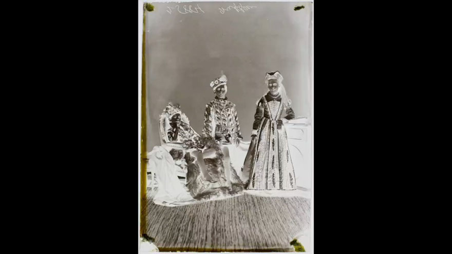 A negative with transmitted light of three costumed children, one seated on the left and the other two standing.