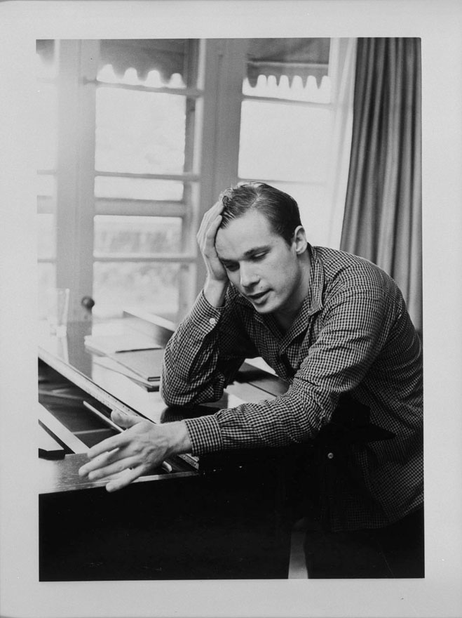 Man leaning on a piano with his elbow, with his head resting on his hand.