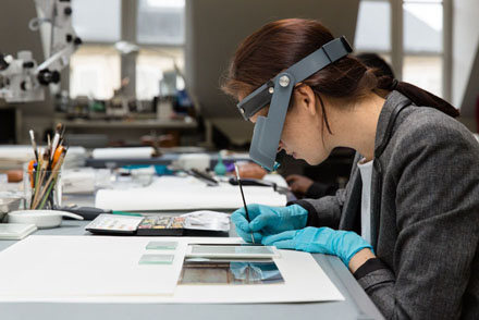 Woman wearing a binocular visor holding a paint brush while treating a photograph.